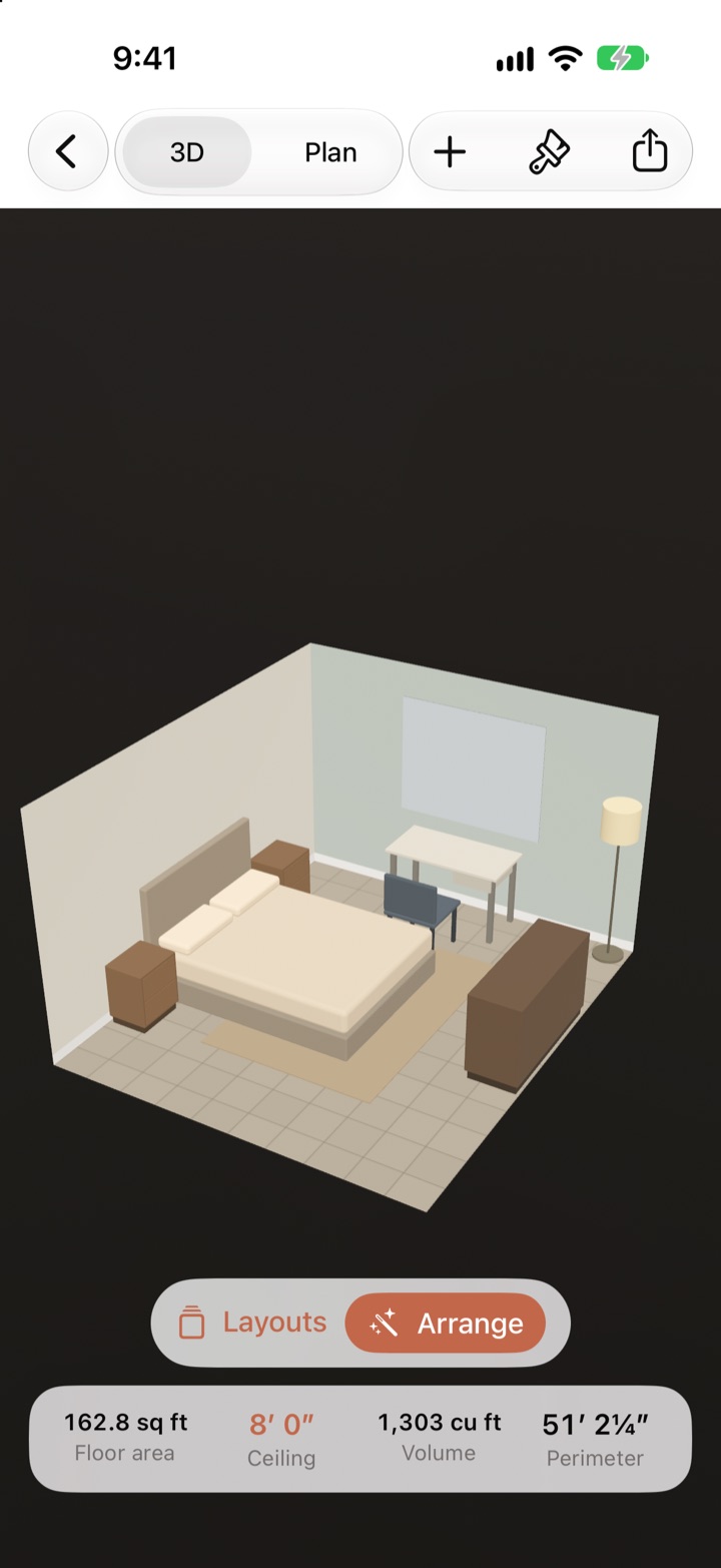 The bedroom in 3D: a bed with a headboard and pillows between two nightstands, a rug, a desk on legs under the window with a chair pulled up to it, a dresser, and a floor lamp, all at their true size and color.